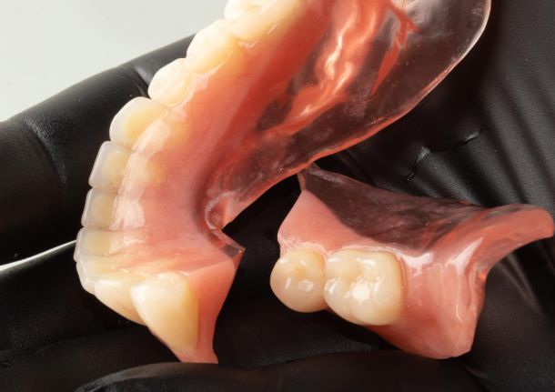 broken denture in the hand of a dental surgeon wearing black rubber gloves